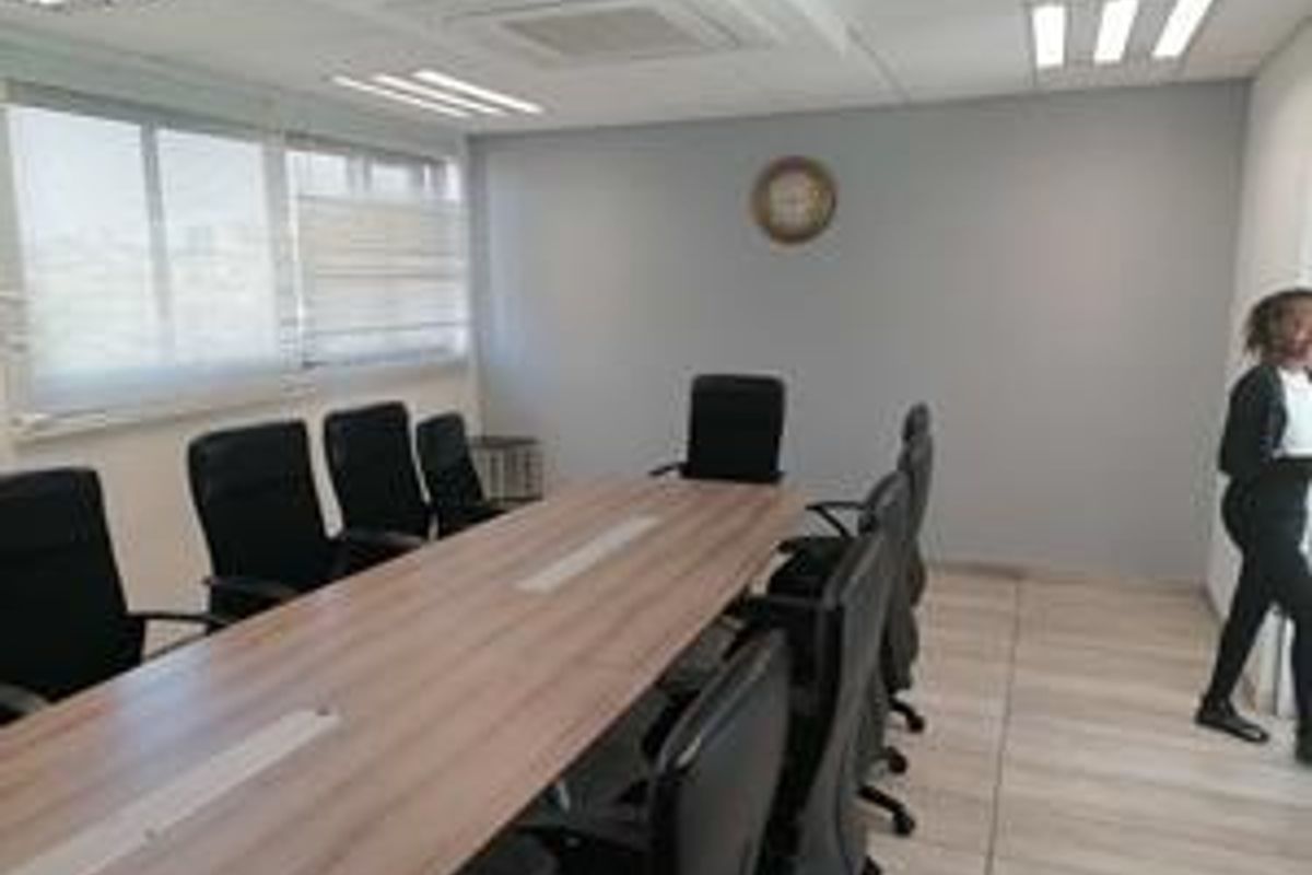 A functional office meeting room featuring a large conference table, recessed ceiling lighting, and large windows providing natural light.