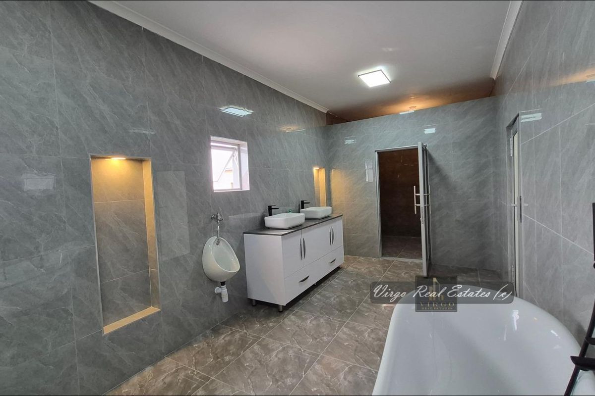 Modern, spacious bathroom featuring grey marble-look tiling, a double vanity with vessel sinks, a wall-mounted urinal, and a contemporary freestanding bathtub.