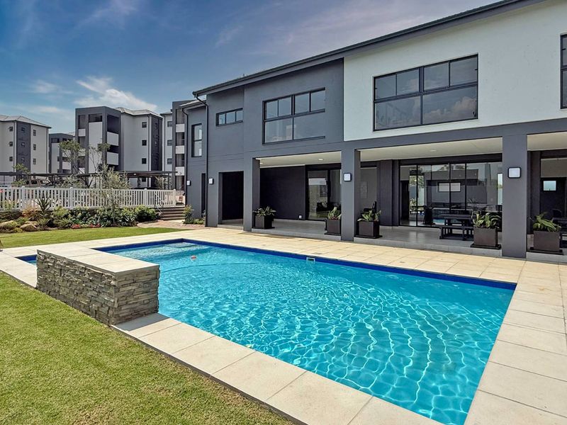 Modern apartment exterior featuring a private swimming pool with stone feature wall, tiled deck, and a spacious covered patio area.