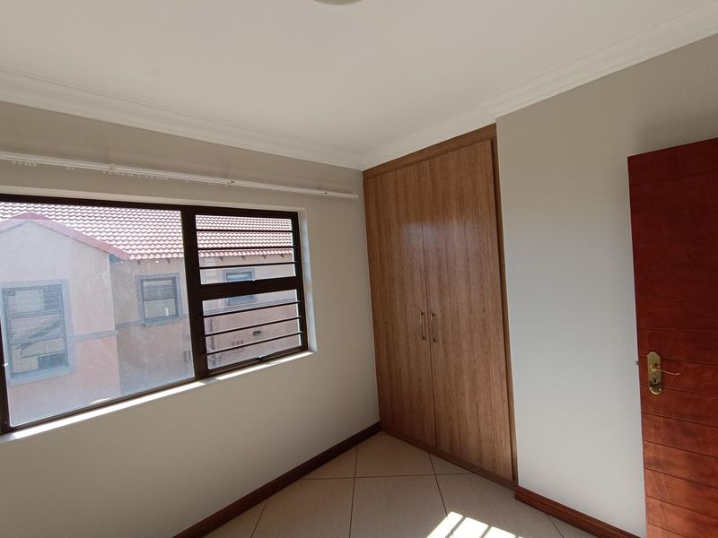 A bright, empty bedroom featuring neutral walls, tiled flooring, and a built-in wooden wardrobe with ample storage space.