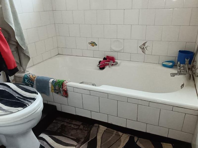 A functional bathroom featuring a standard bathtub and toilet with white wall tiling throughout.