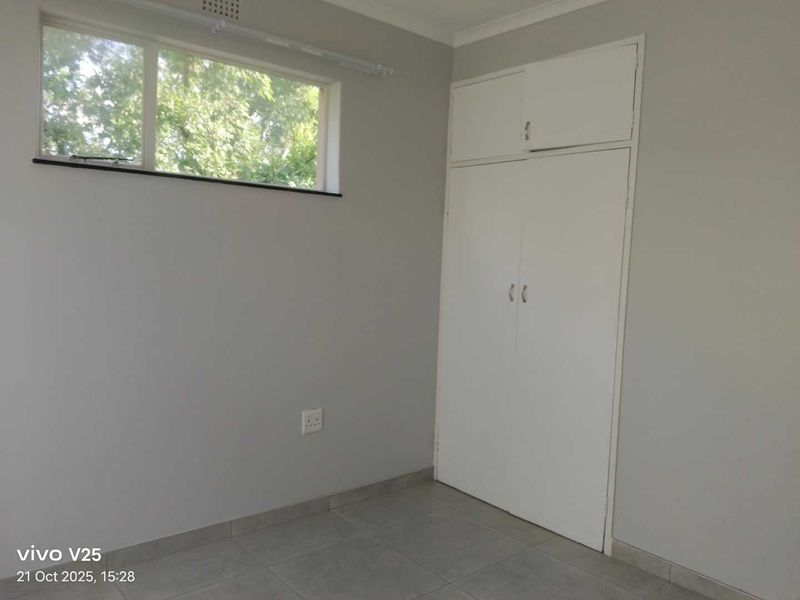 A clean, empty bedroom featuring neutral grey walls, tiled flooring, and a built-in wardrobe with overhead storage.