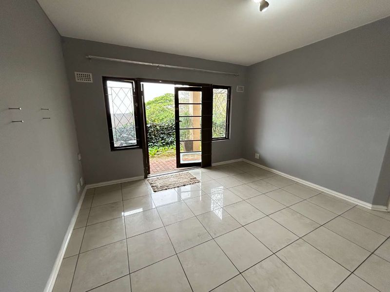 An empty living room featuring neutral grey walls, large format floor tiles, and direct access to an outdoor patio area through glass french doors.