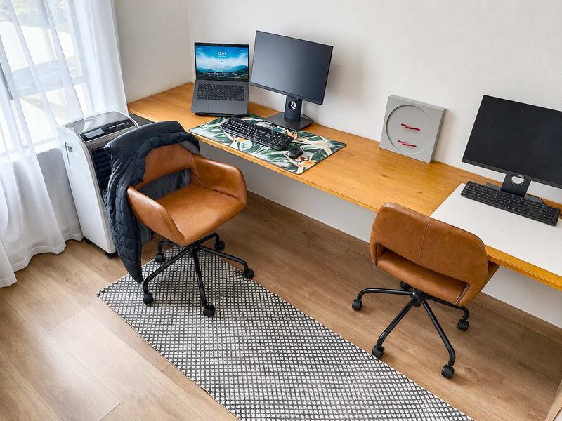 A functional home office space featuring a long, built-in timber desk and modern laminate flooring, providing a clean and organized workspace.