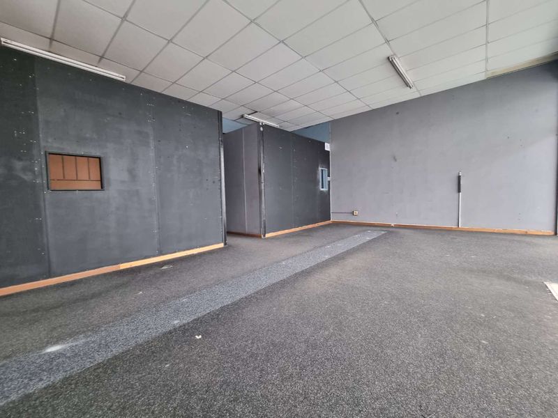 An empty open-plan commercial space featuring suspended ceilings, fluorescent lighting, and dark partition walls, suitable for various business configurations.