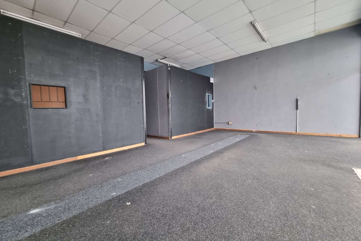 An empty open-plan commercial space featuring suspended ceilings, fluorescent lighting, and dark partition walls, suitable for various business configurations.