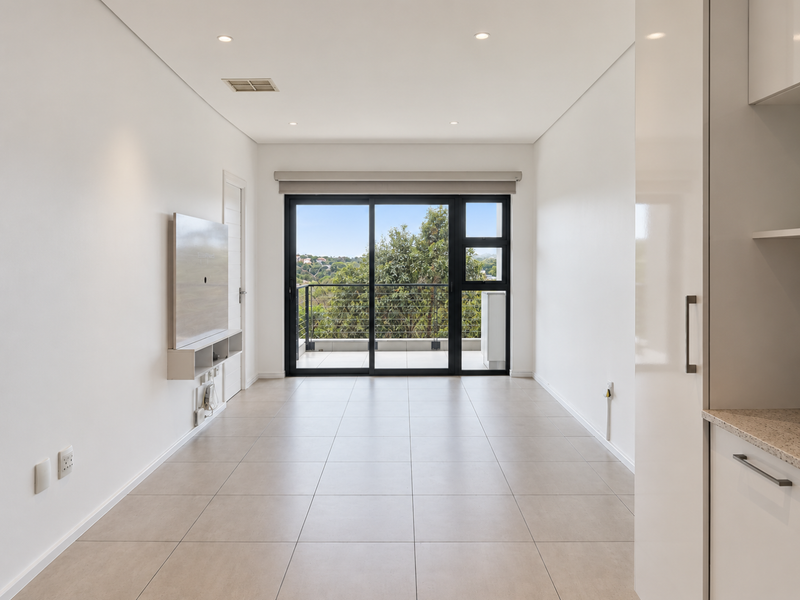 Bright open-plan living area featuring neutral tiled floors, recessed lighting, and a sliding door leading to a private balcony with scenic views.