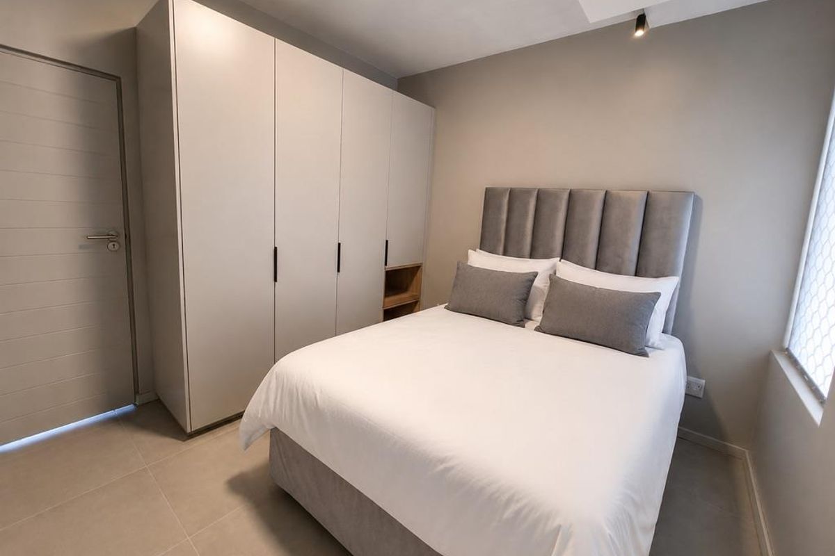 Modern bedroom featuring neutral tones, tiled flooring, and a large built-in wardrobe with integrated shelving.