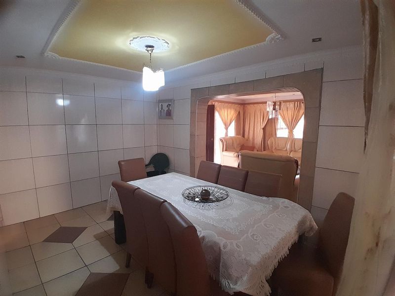 Dining room featuring tiled walls and flooring, a decorative ceiling rose, and an arched opening leading into an adjacent living area.