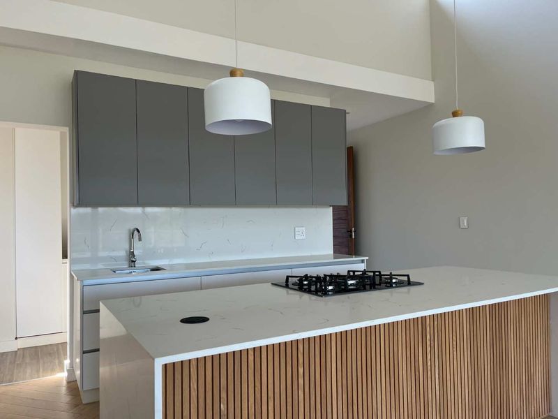 Modern kitchen featuring a central island with a gas hob, quartz countertops, grey cabinetry, and stylish pendant lighting in an open-plan layout.