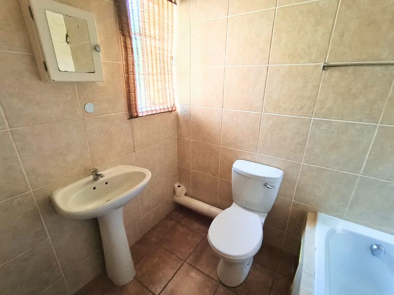 A functional bathroom featuring a pedestal basin, toilet, and bathtub with neutral wall and floor tiling.