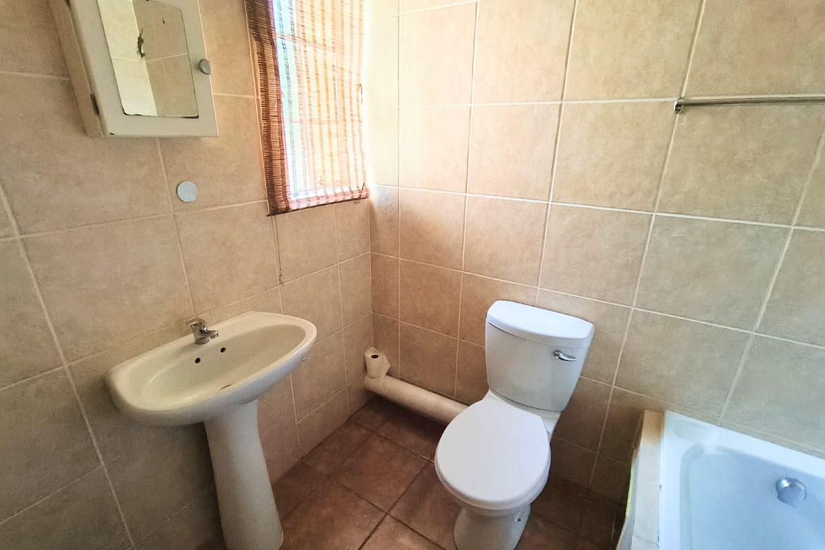 A functional bathroom featuring a pedestal basin, toilet, and bathtub with neutral wall and floor tiling.