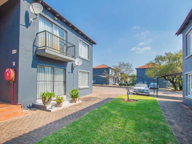 Exterior view of an apartment complex featuring paved driveways, carports, and a balcony with metal railings.