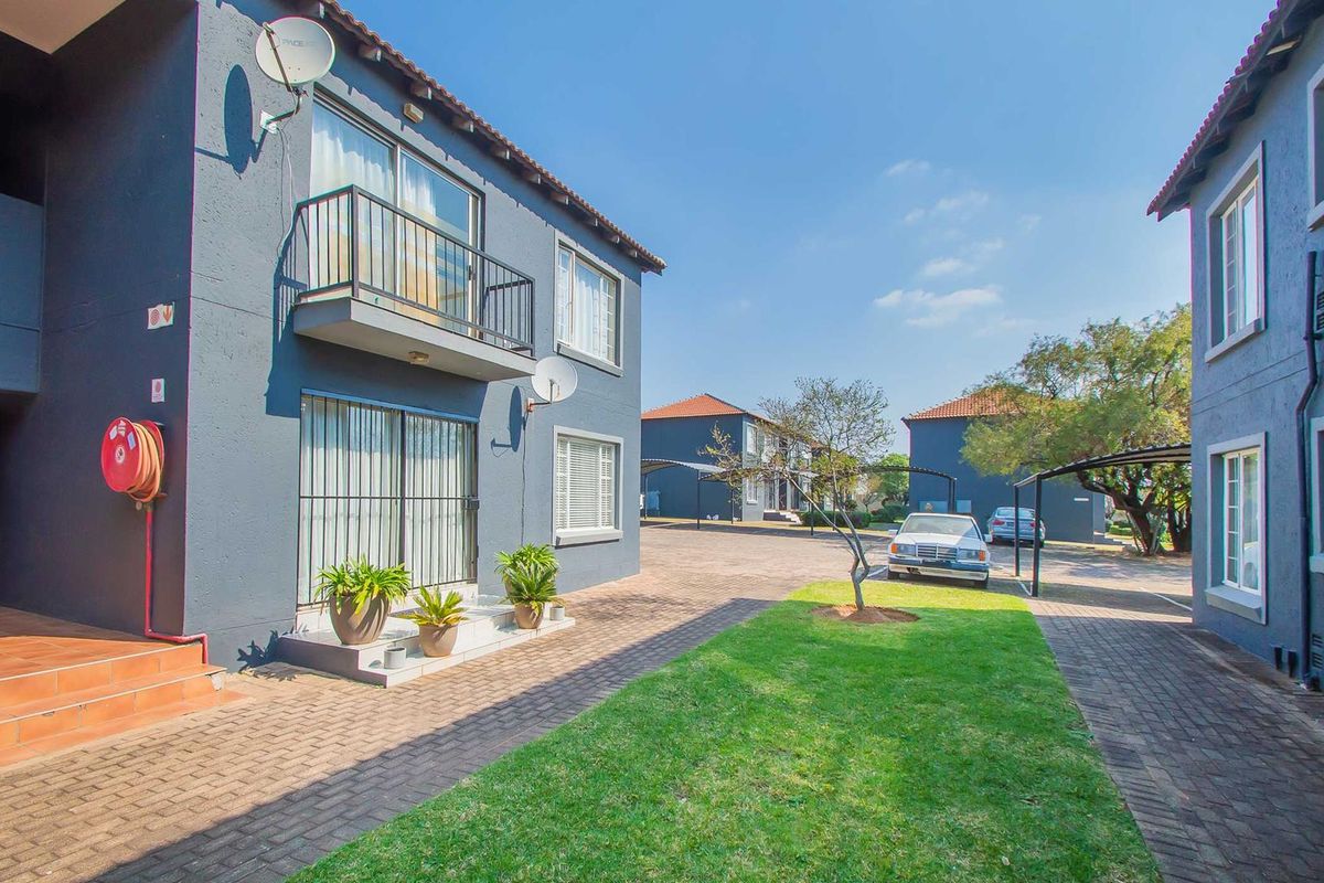 Exterior view of an apartment complex featuring paved driveways, carports, and a balcony with metal railings.