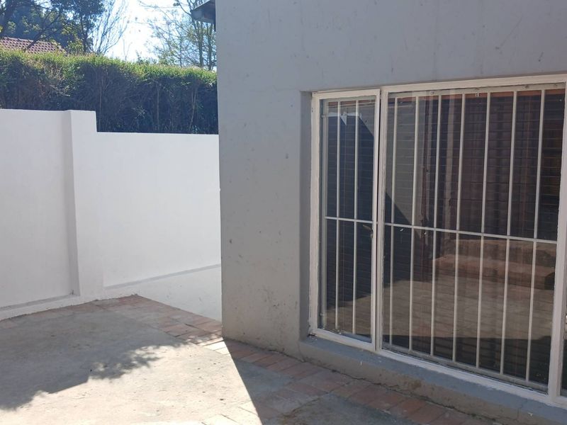 Rear exterior view of the cottage featuring a paved patio area, boundary wall, and sliding glass doors with security bars.