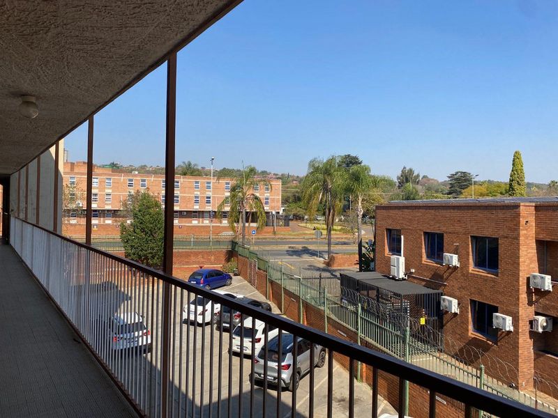 An elevated outdoor balcony walkway overlooking the apartment complex parking area and surrounding neighborhood.