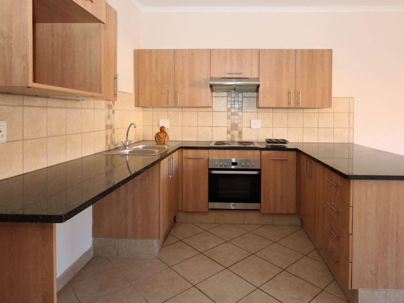 A clean, functional kitchen featuring light wood-finish cabinetry, dark granite countertops, built-in oven, hob, and extractor fan with neutral ceramic tiling.