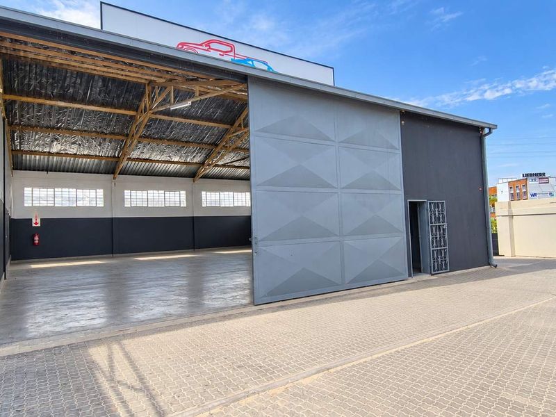 Industrial warehouse facility featuring a large sliding door, concrete flooring, and exposed steel roof trusses, suitable for various commercial or storage operations.