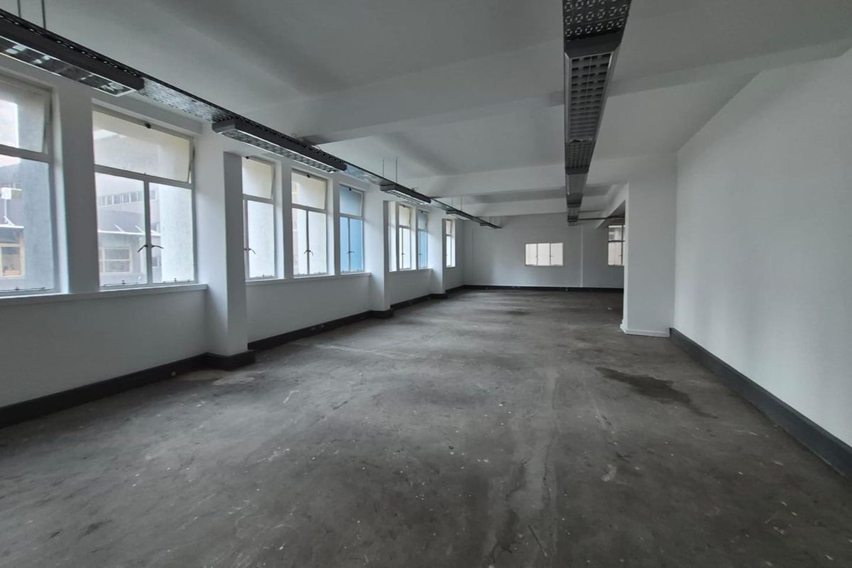 A spacious, vacant open-plan office area featuring large windows, exposed ceiling lighting tracks, and unfinished concrete flooring, ready for custom fit-out.