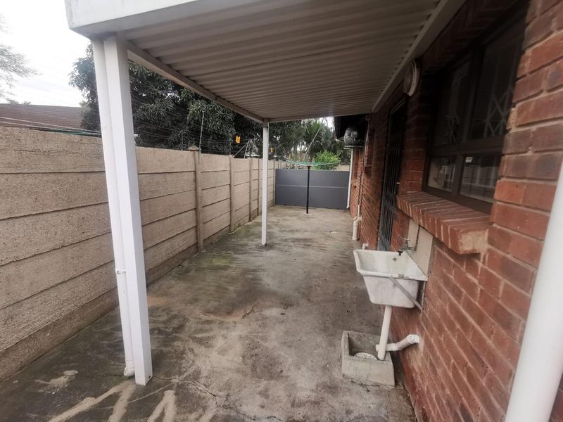 A covered outdoor patio area featuring a brick facade, concrete flooring, and a functional utility sink, providing a practical space for laundry or storage.