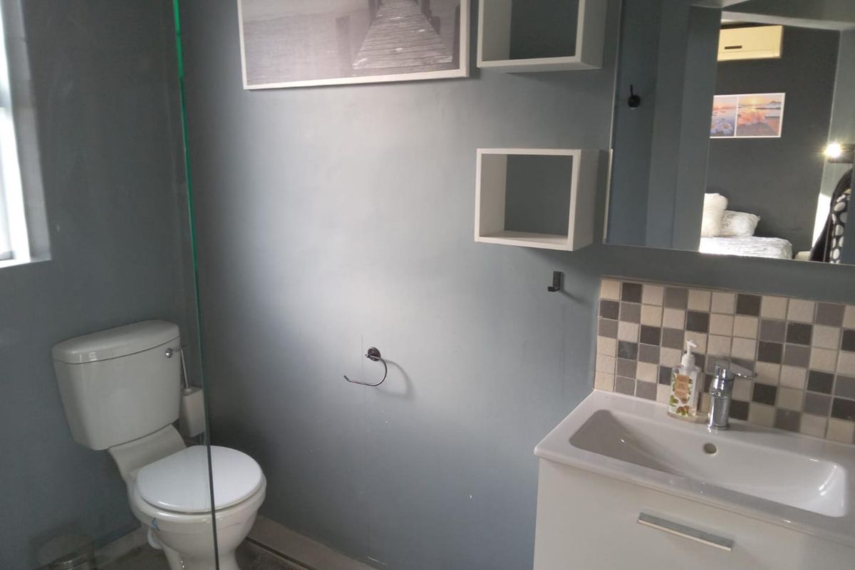 A functional bathroom featuring a vanity with basin, toilet, glass shower screen, and wall-mounted shelving with a tiled splashback.