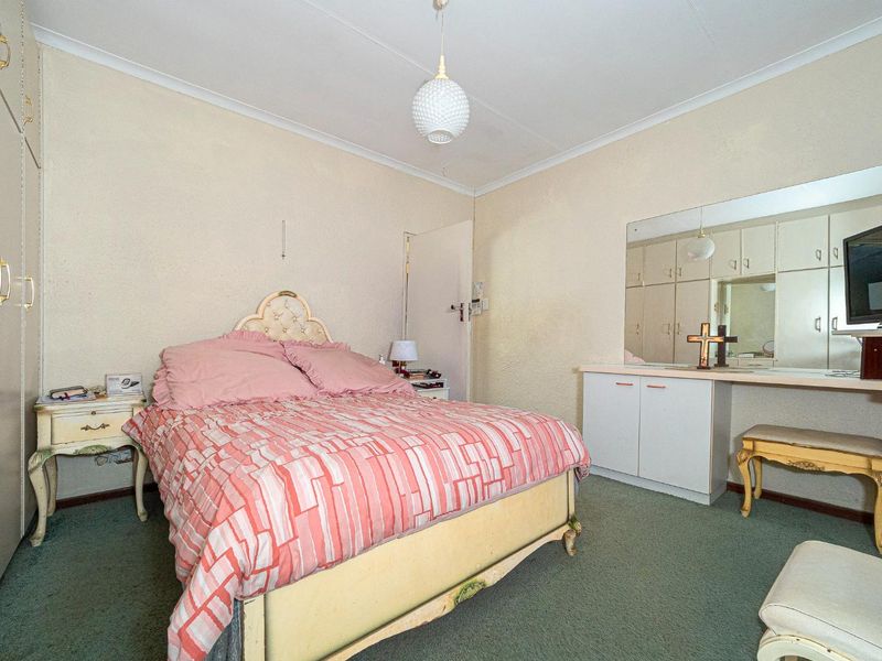 A bedroom featuring built-in cupboards, a vanity area with a large mirror, and carpeted flooring, offering potential for modernization.