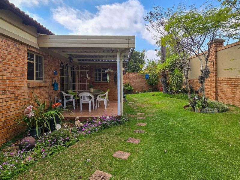 A well-maintained rear garden featuring a covered patio area, brick boundary walls, and a landscaped lawn with a stone pathway.