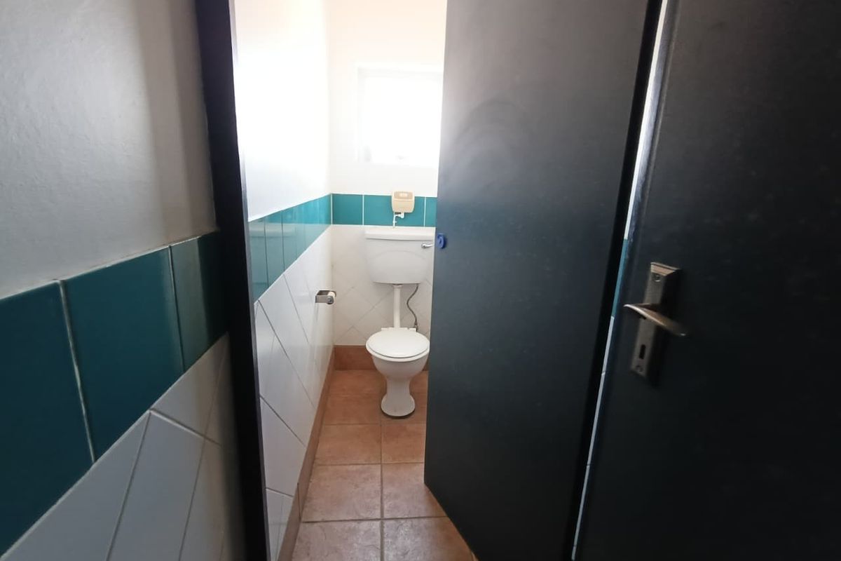 A functional bathroom featuring ceramic wall and floor tiles, equipped with a standard toilet and a privacy door.
