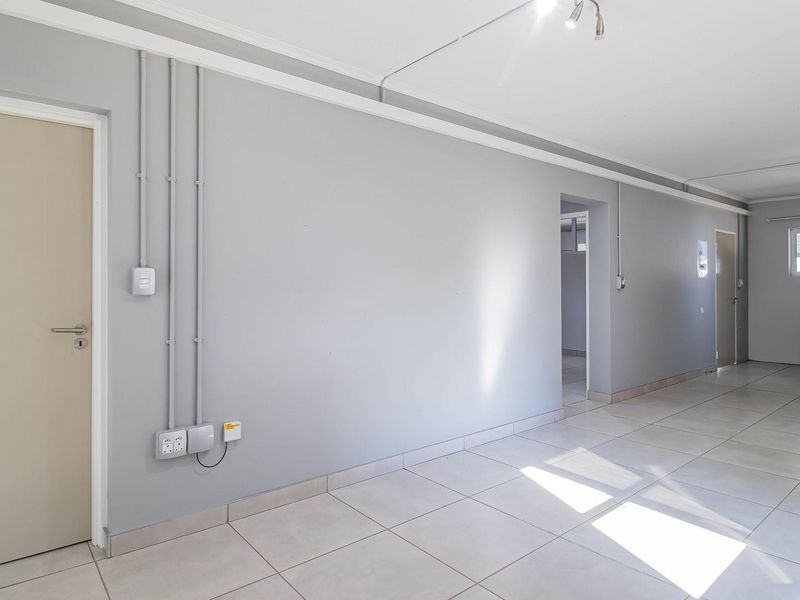 An open-plan living and kitchen area featuring neutral grey walls, tiled flooring, and exposed electrical conduit, offering a clean and functional blank canvas.