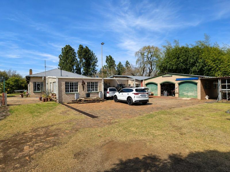 Rear view of the property featuring a brick-paved driveway, double garage, and established garden area with a metal roof structure.