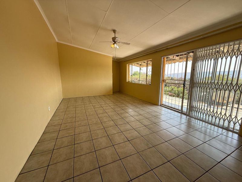 Spacious, empty living area featuring tiled flooring, a ceiling fan, and large sliding glass doors with security gates leading to an outdoor space.