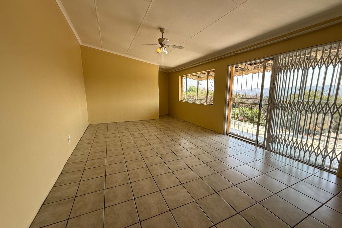 Spacious, empty living area featuring tiled flooring, a ceiling fan, and large sliding glass doors with security gates leading to an outdoor space.