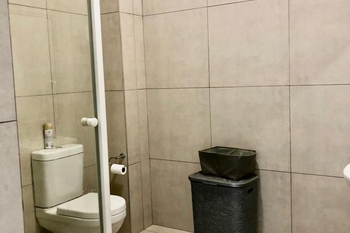 A modern bathroom featuring large-format neutral wall and floor tiles, a glass-enclosed shower, and a standard white toilet suite.