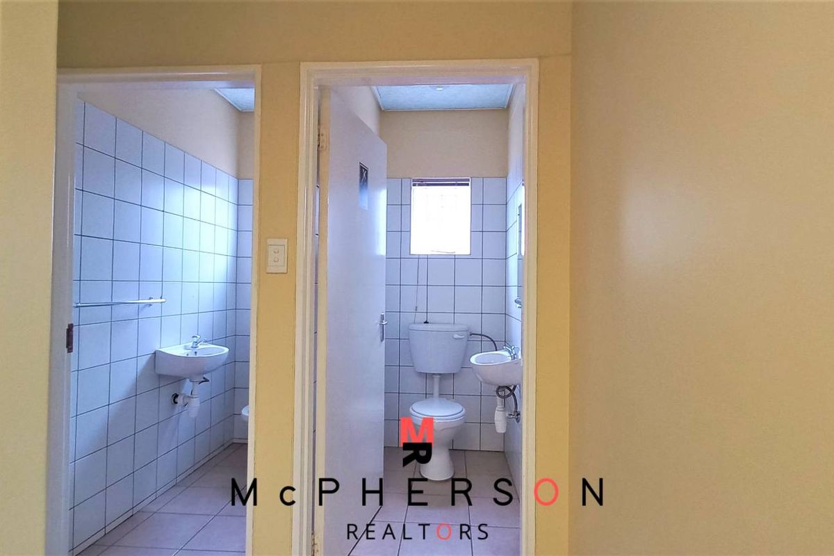 A functional industrial bathroom facility featuring tiled walls, standard ceramic basins, and a toilet, providing essential utility space for the property.