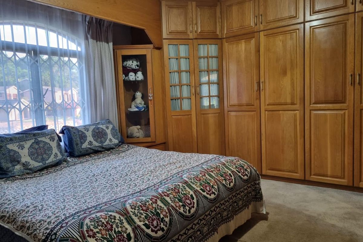 A bedroom featuring extensive built-in wooden cabinetry and wardrobes, providing ample storage space, complemented by a large arched window with security bars.