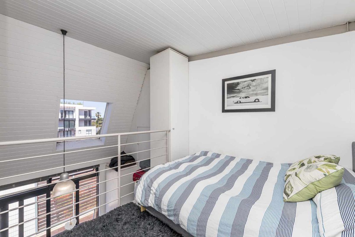 A loft-style bedroom featuring a sloped ceiling, built-in wardrobe, and a metal safety railing overlooking the lower level.