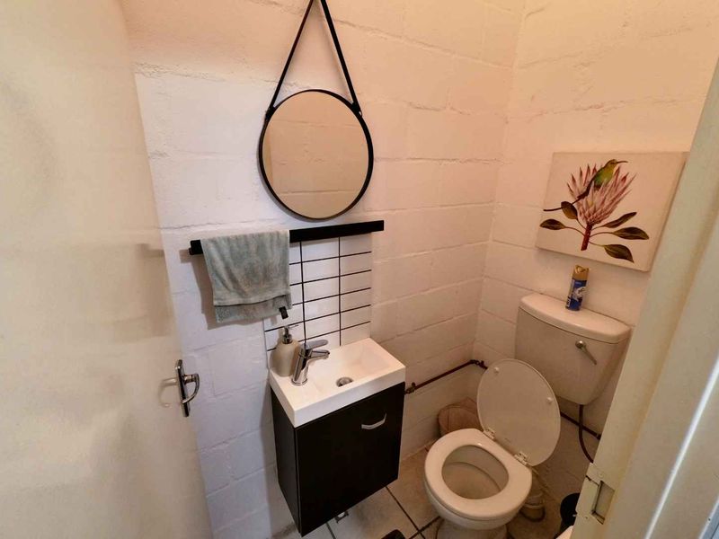 A compact industrial-style bathroom featuring exposed painted brick walls, a modern wall-mounted vanity with basin, and a standard toilet.