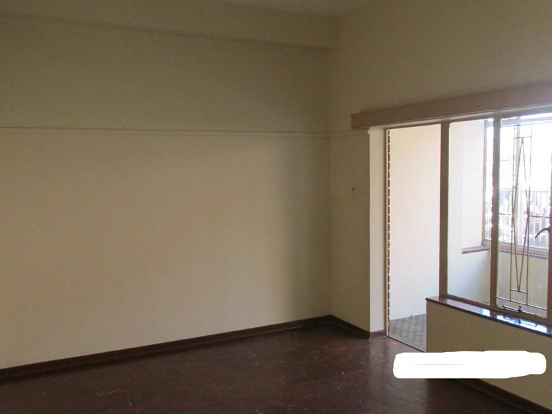 An empty living room featuring large windows with security bars and dark flooring, offering a blank canvas for potential interior design updates.