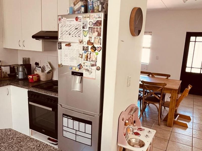 Open-plan kitchen and dining area featuring white cabinetry, granite countertops, built-in oven, extractor fan, and tiled flooring throughout.