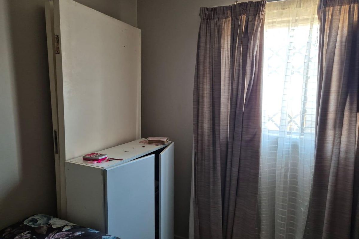 A bedroom featuring a window with curtains and a built-in cupboard unit.