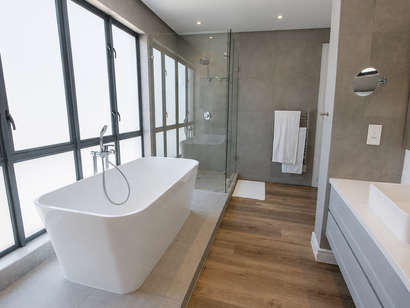 Modern bathroom featuring a sleek freestanding bathtub, glass-enclosed shower, vanity with basin, and high-quality finishes with large windows providing ample natural light.