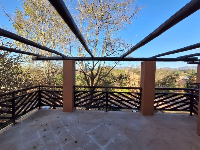 An elevated outdoor balcony featuring a wooden pergola, tiled flooring, and metal balustrades, offering scenic views of the surrounding landscape.