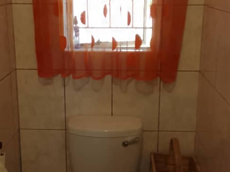 A compact bathroom featuring tiled walls and flooring, equipped with a standard toilet and a window with security bars.