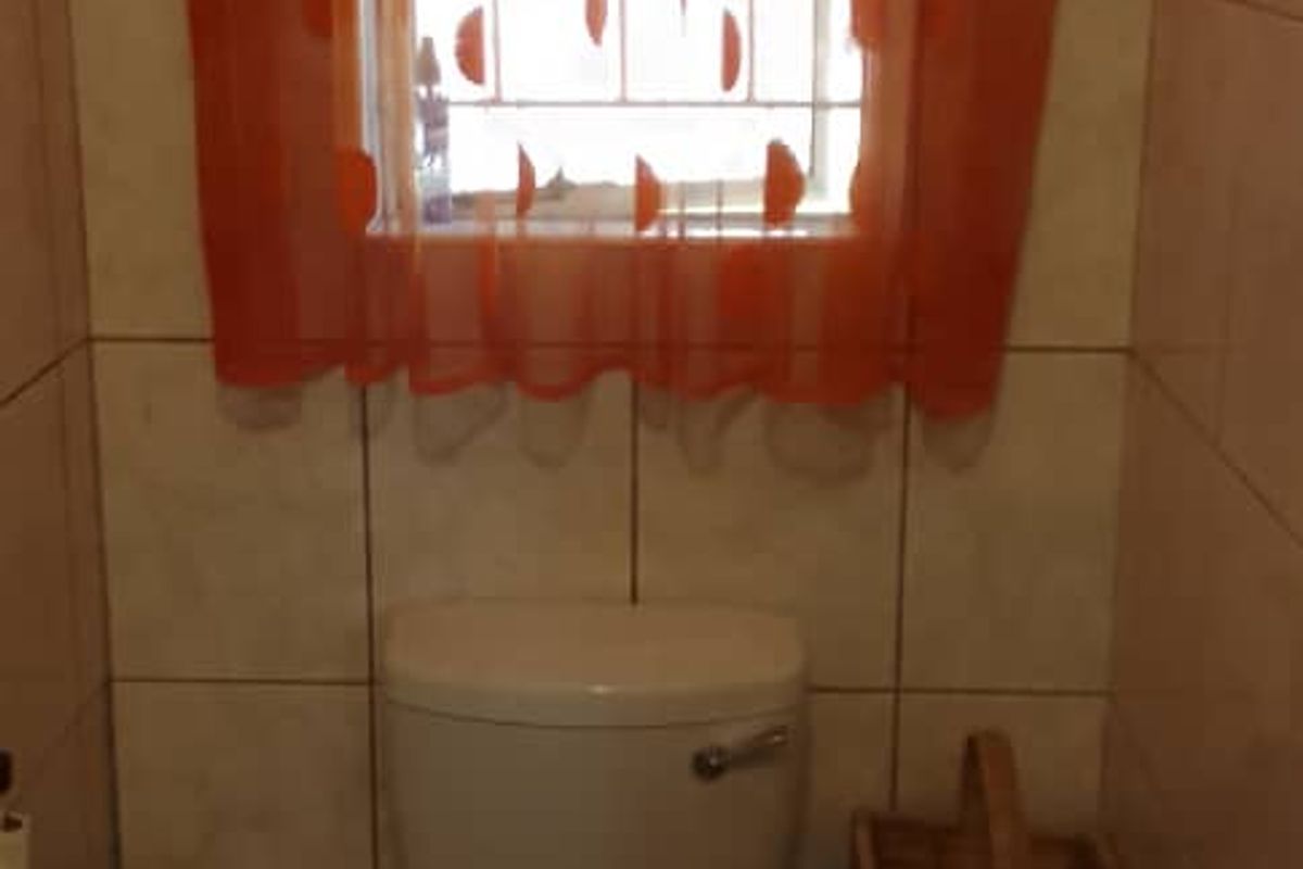 A compact bathroom featuring tiled walls and flooring, equipped with a standard toilet and a window with security bars.