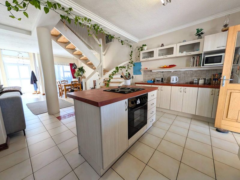 Open-plan kitchen featuring a central island with built-in oven and hob, tiled flooring, and an adjacent staircase leading to the upper level.