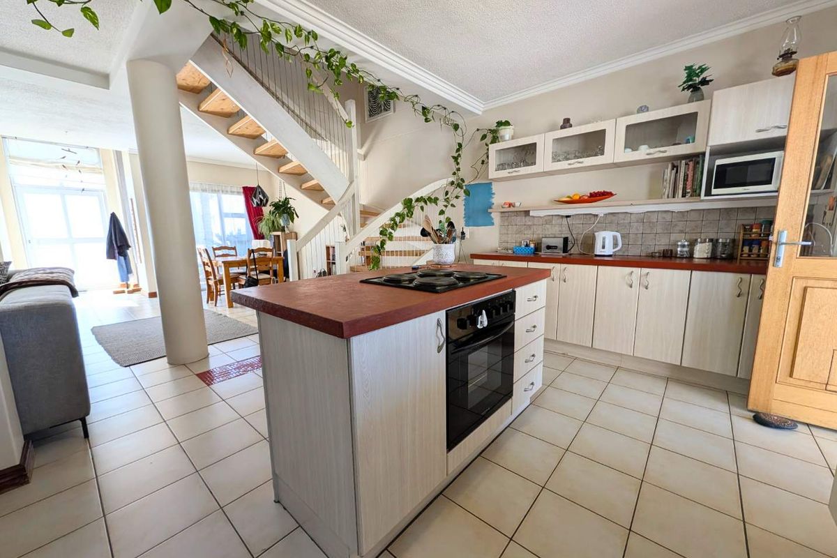 Open-plan kitchen featuring a central island with built-in oven and hob, tiled flooring, and an adjacent staircase leading to the upper level.
