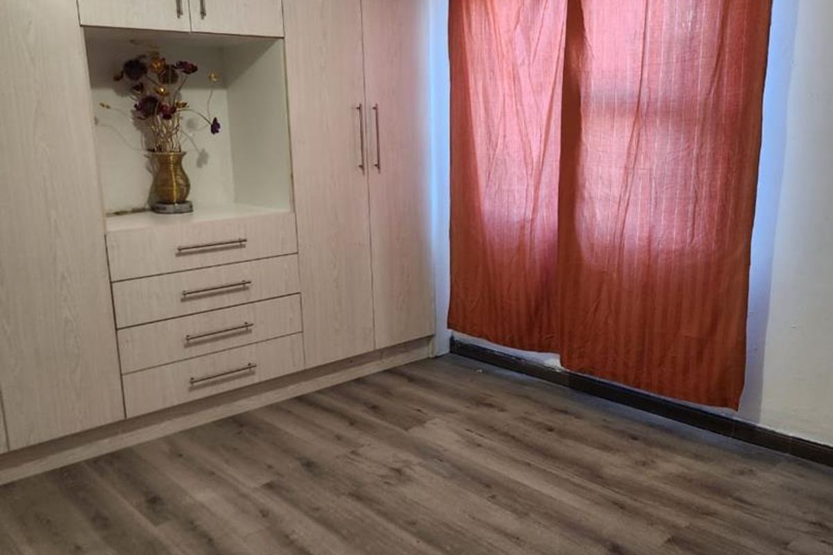 A bedroom featuring light wood-grain built-in cabinetry with integrated drawers and shelving, complemented by modern wood-look laminate flooring.