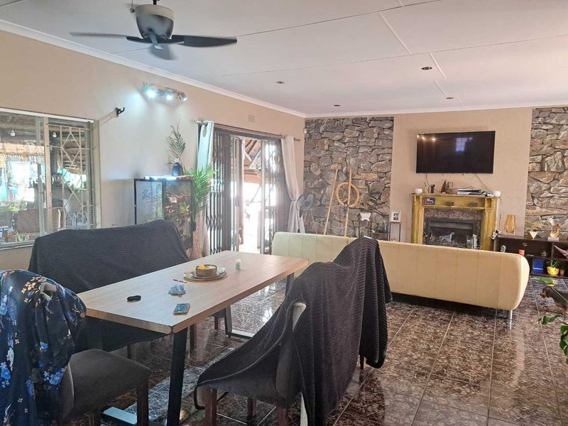 Spacious open-plan living and dining area featuring a striking stone fireplace wall, tiled flooring, and direct access to the outdoor patio through sliding doors.