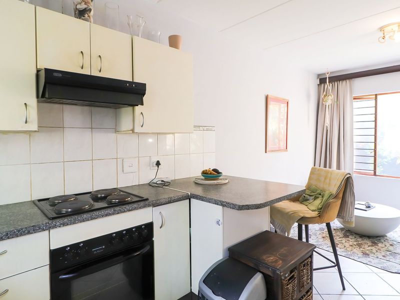 Open-plan kitchen and living area featuring built-in cabinetry, electric hob, oven, and tiled flooring, offering a functional layout for modern apartment living.
