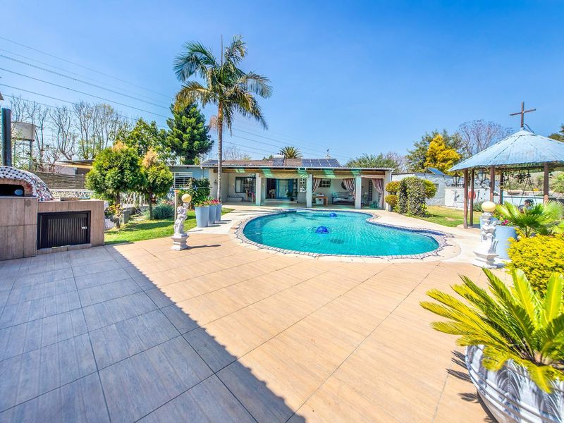 Outdoor entertainment area featuring a swimming pool, tiled patio, built-in pizza oven, and a gazebo set within a landscaped garden.